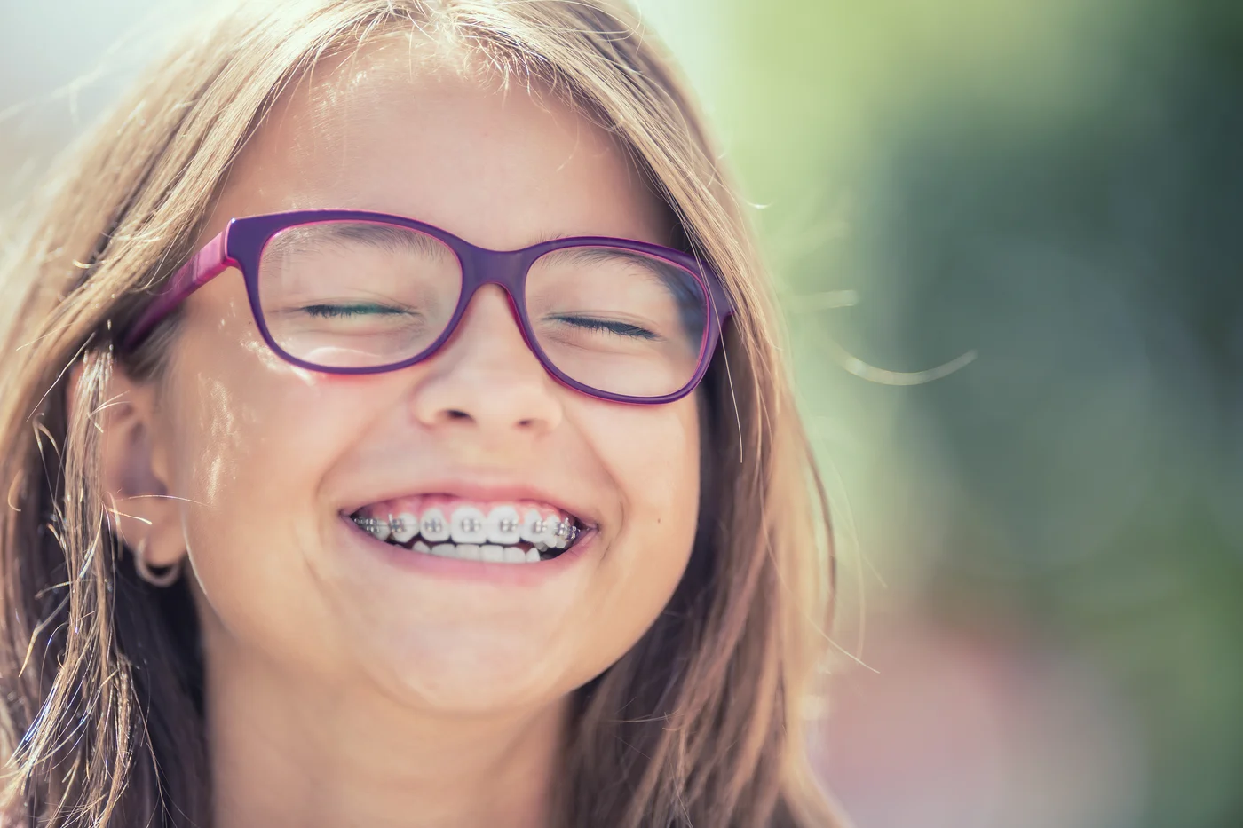 Smiling girl wearing purple glasses and braces outdoors