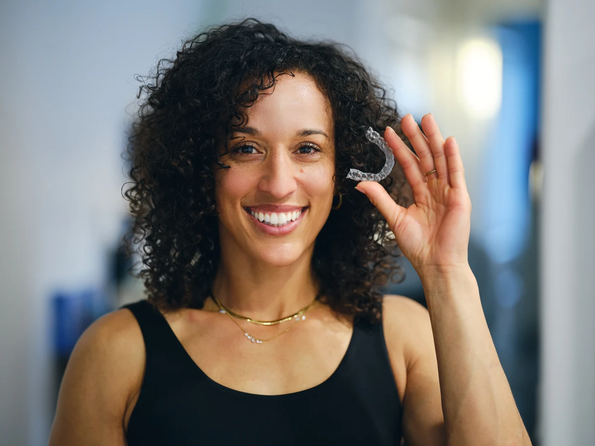 Smiling woman holding a clear orthodontic aligner